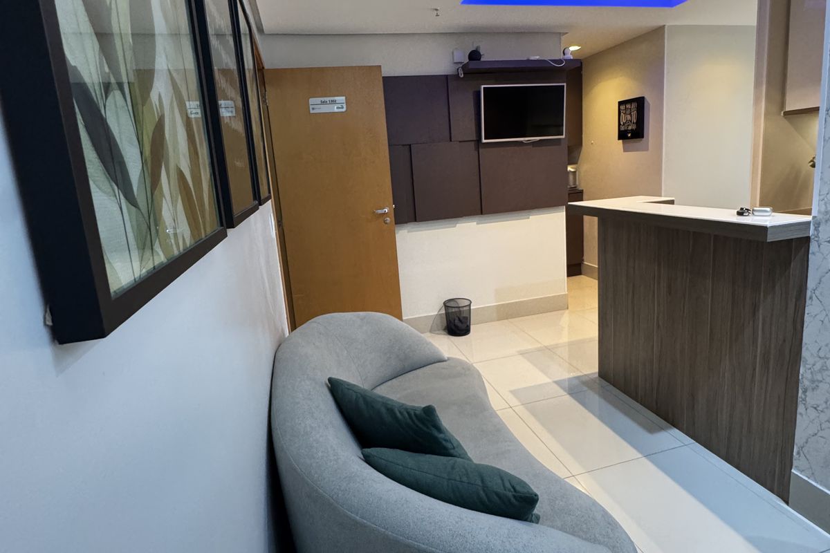 Sala de espera com sofá confortável e balcão da recepção ao fundo